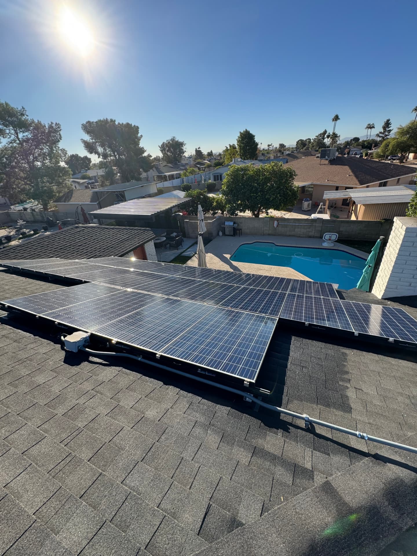 Clean solar array on a shingle roof above a backyard pool