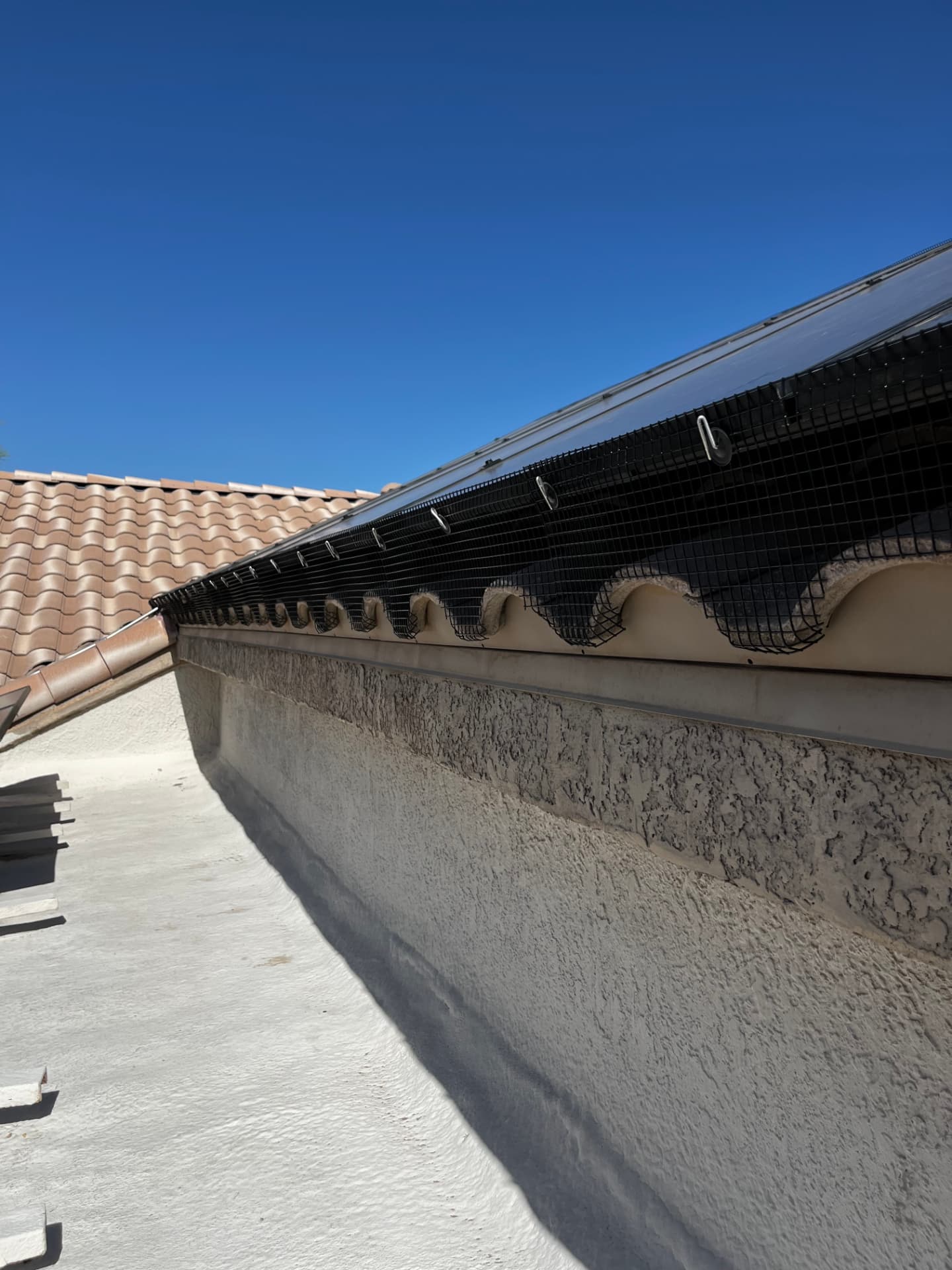 Mesh barrier running along a solar array above a stucco parapet